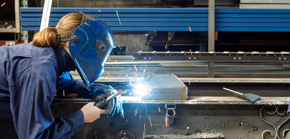 Young Female Welder Working In Factory Wearing Protective Safety Gear