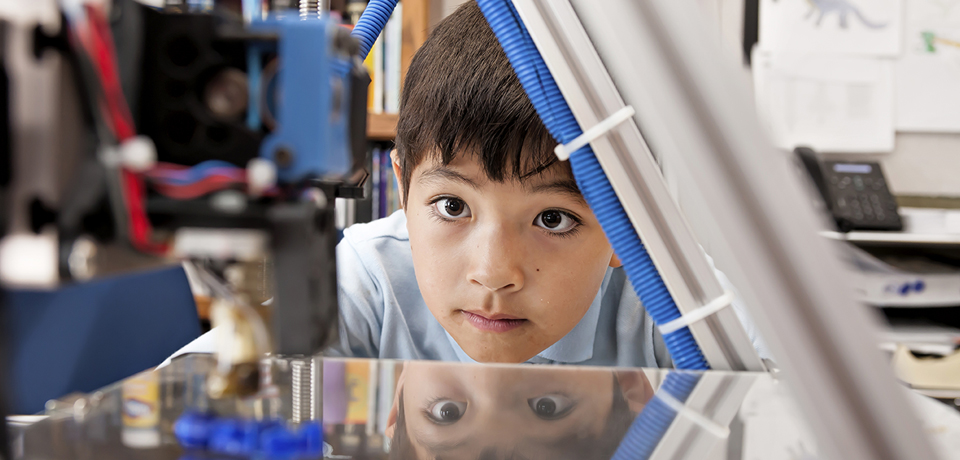 A young boy watches as a 3D printer prints an object.